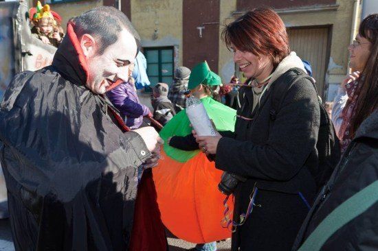 Ein Mann in einem Vampirkostüm reicht einer Frau in einem schwarzen Mantel eine Kürbis bei einem Straßenfest.