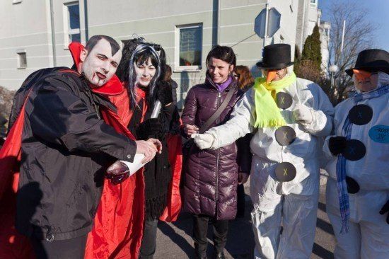 Eine Gruppe von Menschen in Kostümen, darunter Dracula, eine Hexe und zwei Schneemänner, stehen vor einem Gebäude.