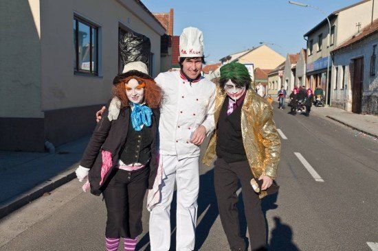 Drei Menschen in Kostümen stehen auf der Straße, wobei eine Person eine Kochmütze trägt und die anderen beiden Schminke und Kostüme tragen.