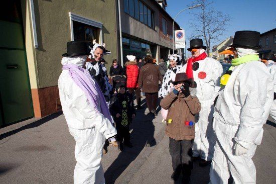 Eine Gruppe von Menschen in verschiedenen Kostümen, darunter Schneemänner, geht auf einer Straße. Ein Kind hält eine Kamera.