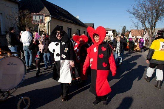 Ein Straßenumzug mit Menschen in Kostümen, einer als Joker und der andere als Pik Dame. Ein Schlagzeug ist links.