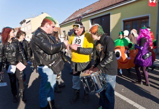 Eine Gruppe von Menschen in bunten Kostümen steht auf der Straße, einer von ihnen hält eine Trommel und ein anderer ein Stück Papier.