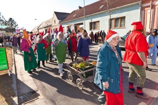 Eine Gruppe von Menschen in verschiedenen Kostümen, einschließlich Weihnachtsmützen, geht die Straße entlang. Eine Frau vorne schiebt einen Wagen mit Blumen.