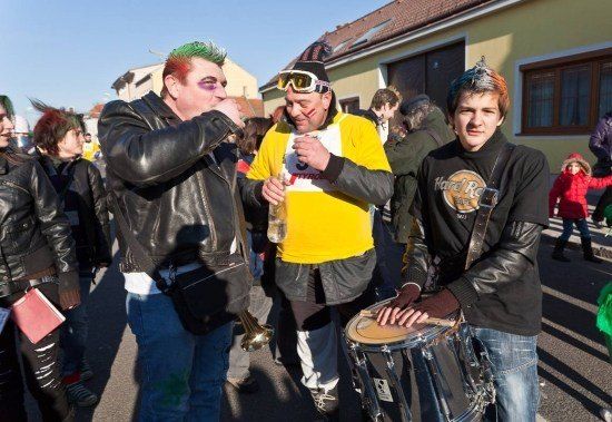 Eine Gruppe von Menschen in Punk- und Karnevalskostümen geht auf der Straße, einer hält eine Trompete und ein anderer spielt eine Trommel.