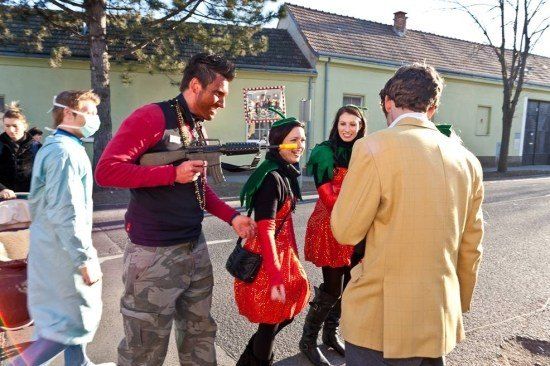 Eine Gruppe von Menschen in Kostümen, einer hält eine Spielzeugpistole, geht auf einer Straße mit Gebäuden im Hintergrund.