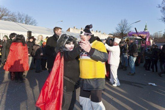 Eine Gruppe von Menschen in Kostümen, eine Frau in einem roten Umhang und eine andere in einem gelben Shirt, stehen auf einer Straße während eines Festivals.