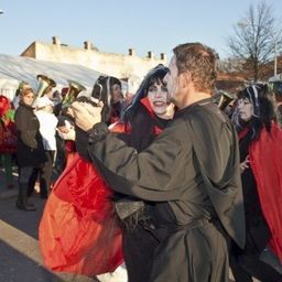 Ein Mann und eine Frau in Kostümen tanzen auf der Straße, während eine Menschenmenge zuschaut.