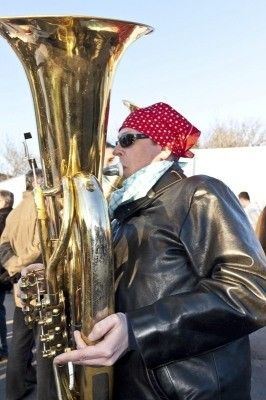 Ein Mann mit rotem Bandana und Sonnenbrille spielt eine große Messingtuba im Freien.