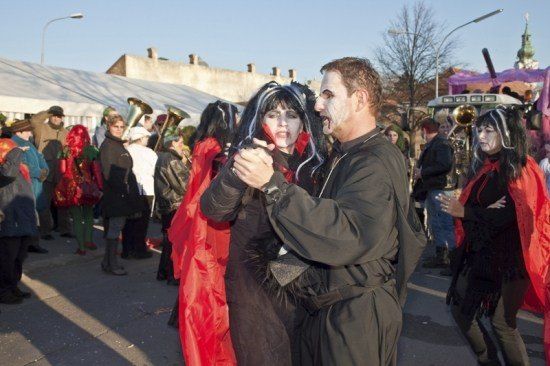 Ein Mann und eine Frau in Vampirkostümen tanzen bei einer Halloween-Veranstaltung, umgeben von anderen kostümierten Personen und einer festlichen Atmosphäre.