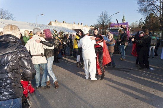 Eine Gruppe von Menschen in Kostümen tanzt auf der Straße, mit einer Band, die hinter ihnen spielt.