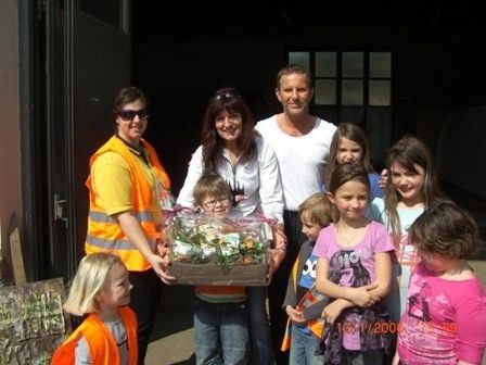 Eine Gruppe von Menschen, einschließlich Erwachsener und Kindern, steht zusammen und posiert für ein Foto. Die Erwachsenen halten eine Box mit Blumen und Pflanzen. Die Kinder tragen verschiedenfarbige Hemden. Das Foto wurde 2006 aufgenommen.