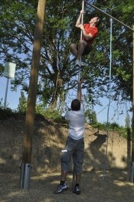 Ein Mann klettert an einem Seil, während ein anderer Mann das Seil von unten hält an einem sonnigen Tag.