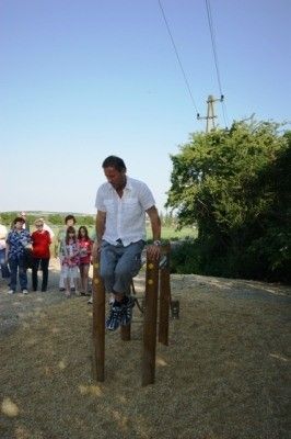 Ein Mann führt Klimmzüge an einem Holzbalken in einem Park durch, während mehrere Menschen im Hintergrund zusehen.