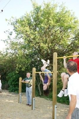 Eine Gruppe von Menschen macht Klimmzüge an Outdoor-Stangen in einem Park mit Bäumen im Hintergrund.