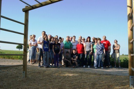 Eine Gruppe von Menschen steht in einem Feld mit einer Holzstruktur hinter ihnen. Sie alle lächeln und scheinen für ein Foto zu posieren.
