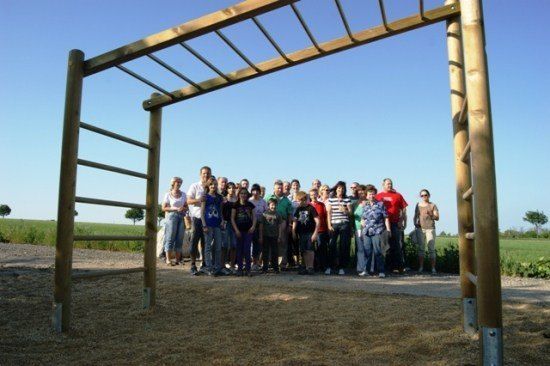 Eine Gruppe von Menschen steht an einem sonnigen Tag vor einem hölzernen Hindernisparcours.