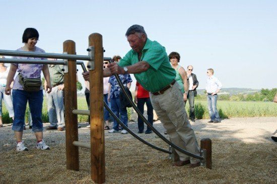 Ein älterer Mann benutzt ein Gerät für Outdoor-Training, während eine Gruppe von Menschen zuschaut.