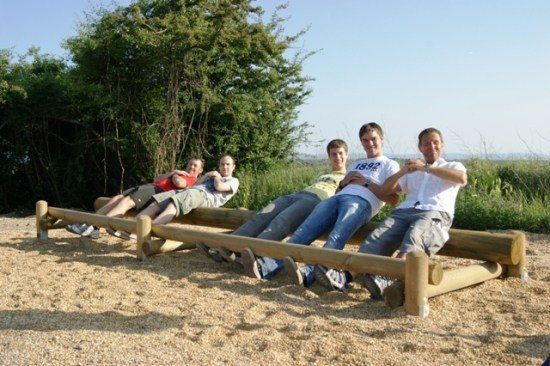 Fünf Männer sitzen auf einer Holzbank in einem Park und posieren für ein Foto mit einem klaren blauen Himmel im Hintergrund.
