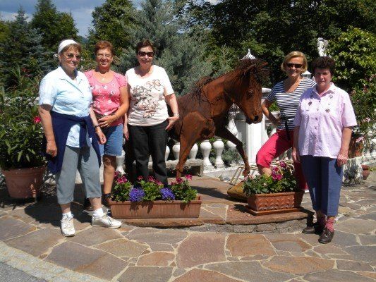 Fünf Frauen stehen vor einem Garten mit einer großen Metallpferdestatue und posieren lächelnd für ein Foto.