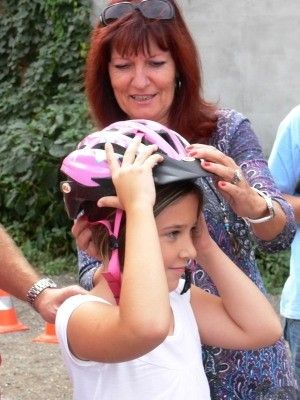 Eine Frau hilft einem jungen Mädchen, einen rosa und schwarzen Fahrradhelm auf dem Kopf anzupassen.