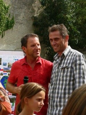 Zwei Männer und ein Mädchen stehen draußen. Der Mann auf der linken Seite hält ein Mikrofon. Der Mann auf der rechten Seite trägt ein kariertes Hemd. Das Mädchen hat lange Haare. Sie stehen vor einer Wand.