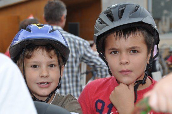 Zwei junge Jungen in Helmen, einer trägt einen blauen Helm und der andere einen grauen Helm, stehen zusammen in einer Außenumgebung.