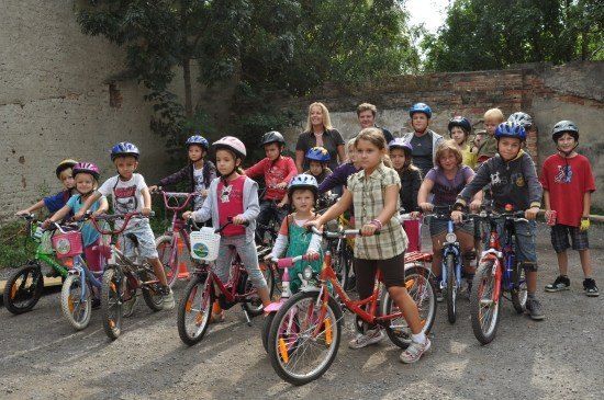 Eine Gruppe von Kindern und Erwachsenen posiert mit ihren Fahrrädern vor einer Ziegelmauer für ein Foto.