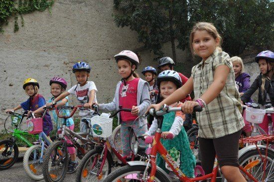 Eine Gruppe von Kindern mit Helmen und Fahrrädern in einer Reihe auf einer Straße.