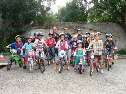 Eine Gruppe von Kindern und Erwachsenen mit Helmen posiert für ein Foto mit ihren Fahrrädern vor einer Ziegelmauer.