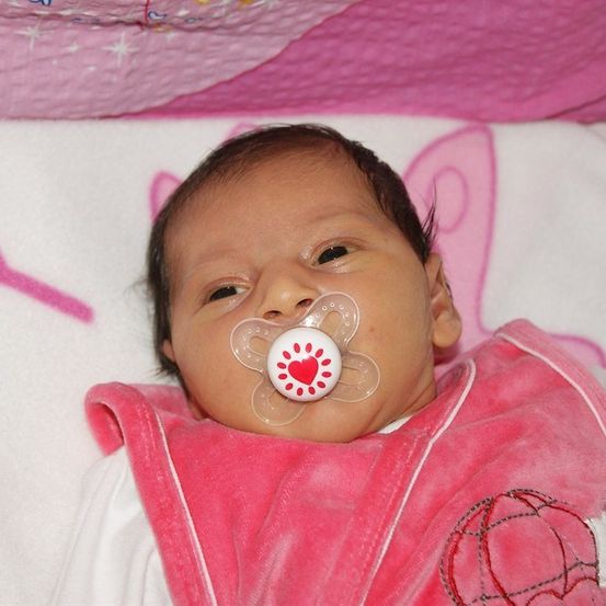 Ein Babymädchen mit einem Schnuller mit Herzdesign liegt auf einer rosa Decke.
