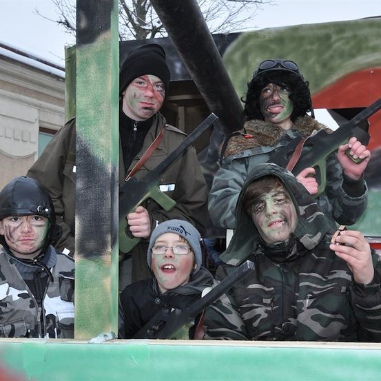 Fünf Personen in militärischen Tarnkostümen mit grüner Gesichtsbemalung posieren mit Spielzeugwaffen vor einem Gebäude.