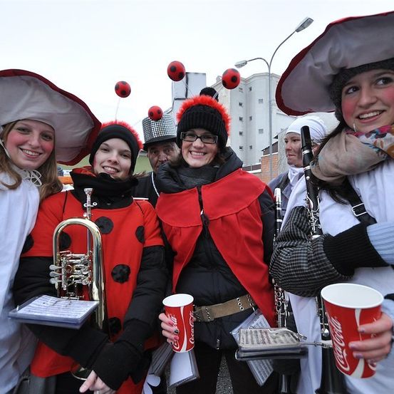 Eine Gruppe von Menschen in roten und schwarzen Kostümen mit ladybug-inspirierten Accessoires, die Musikinstrumente und Coca-Cola-Becher halten, posiert für ein Foto.