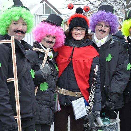 Fünf Menschen in farbenfrohen Perücken und Kostümen, möglicherweise für ein Fest, stehen zusammen, einer hält ein Musikinstrument.