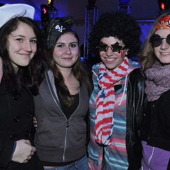 Vier Frauen in verschiedenen Kostümen posieren für ein Foto auf einer Party. Die Frau auf der linken Seite trägt eine weiße Kochmütze, während die Frau neben ihr eine Piratenmütze trägt. Die Frau in der Mitte trägt ein gestreiftes Hemd und eine Krawatte. Die Frau auf der rechten Seite trägt eine Sonnenbrille und eine Stirnband.