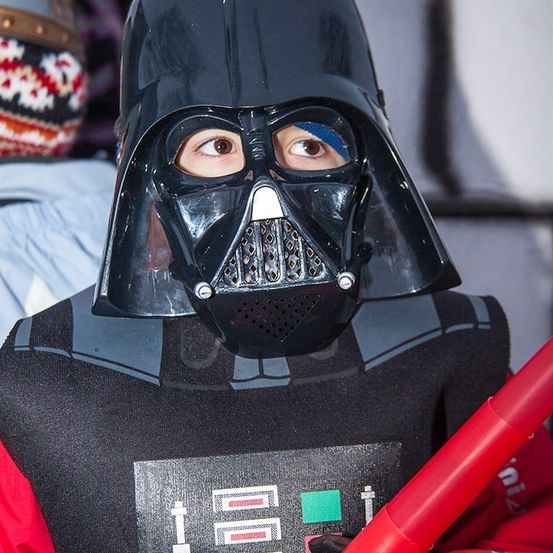 Ein Kind verkleidet als Darth Vader aus Star Wars, hält ein rotes Lichtschwert.