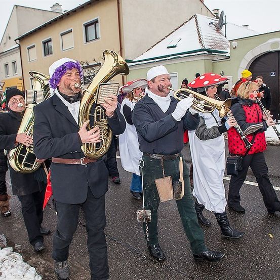 Eine Gruppe von Musikern in Kostümen spielt Instrumente bei einem Umzug auf einer verschneiten Straße.