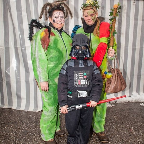 Drei Personen in Kostümen, eine als Hexe, eine als Sturmtruppler und eine als Kind verkleidet als Darth Vader, posieren für ein Foto.