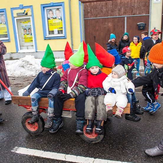 Eine Gruppe von Kindern in Elfenhüten fährt in einem Holzwagen auf einer verschneiten Straße.