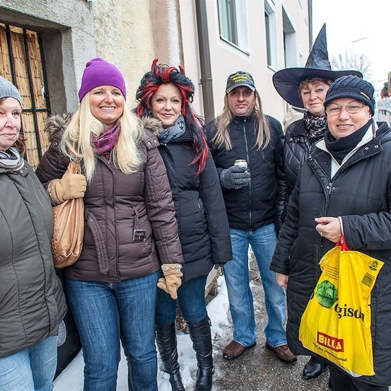 Fünf Erwachsene in Winterkleidung und Hüten stehen zusammen draußen in einem verschneiten Bereich. Eine Frau hält einen gelben Beutel mit dem Wort Billa darauf.