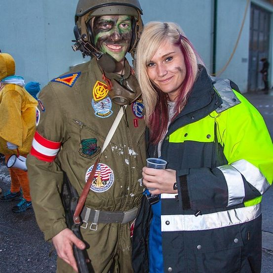 Ein Mann in einer Militäruniform mit grüner Gesichtsbemalung und einer Frau in einer neonfarbenen Jacke, die einen Becher hält.