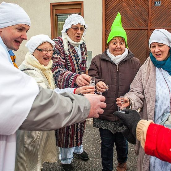 Eine Gruppe von Menschen in Winterkleidung und Hüten, einige mit Gläsern in der Hand, scheinen ein Ereignis vor einem Gebäude zu feiern.