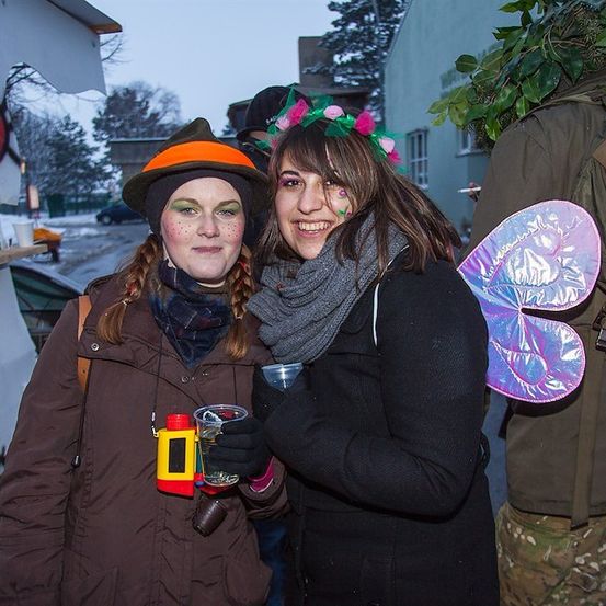 Zwei Frauen in Kostümen, eine mit einem Schmetterlingsflügel und die andere mit einem Hut, stehen draußen im Winter.
