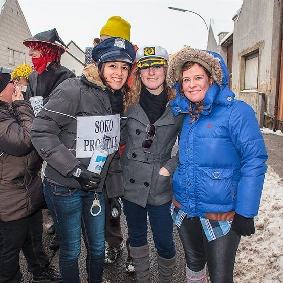 Eine Gruppe von Frauen in Winterkleidung und Mützen steht auf einer verschneiten Straße und lächelt für ein Foto. Eine Frau hält ein Schild mit der Aufschrift 'SOKO PROVILE'.