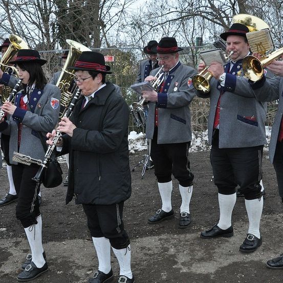 Eine Gruppe von Musikern in traditioneller Kleidung, die Blech- und Holzblasinstrumente im Freien spielen.