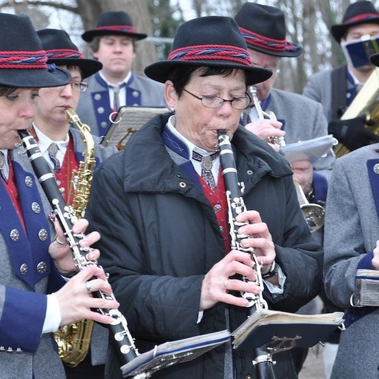 Eine Gruppe von Musikern in passenden Uniformen spielt verschiedene Instrumente, darunter Klarinetten, Saxophone und Trompeten, in einer Außenumgebung.