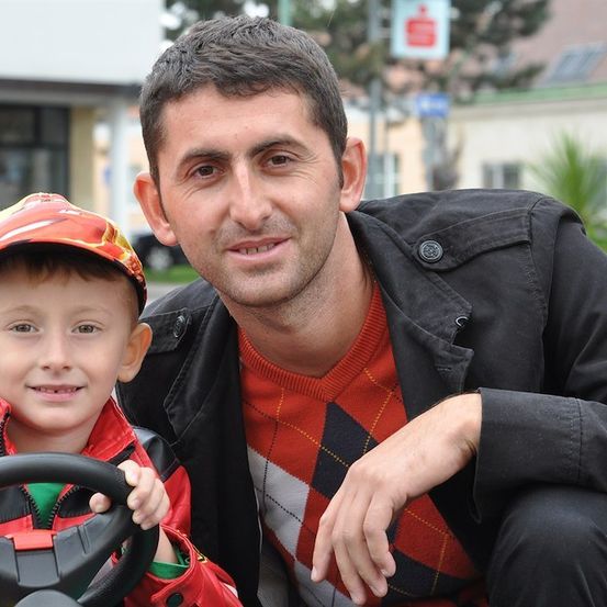 Ein Mann und ein kleiner Junge posieren für ein Foto. Der Junge hält ein Spielzeug-Lenkrad. Sie lächeln beide.