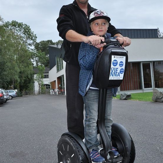 Ein Mann hält einen kleinen Jungen auf einem Segway in einem Parkplatz.