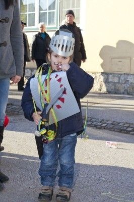 Ein kleiner Junge, der als Ritter verkleidet ist, mit Helm und Schwert, steht auf der Straße.