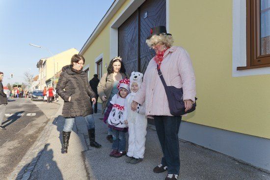 Eine Gruppe von Menschen, darunter zwei Kinder in Kostümen, geht vor einem gelben Gebäude auf der Straße.