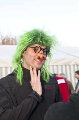 Ein Mann mit grünen Haaren und einer roten Nase, der eine Brille und eine schwarze Jacke trägt, lächelt und posiert für ein Foto.